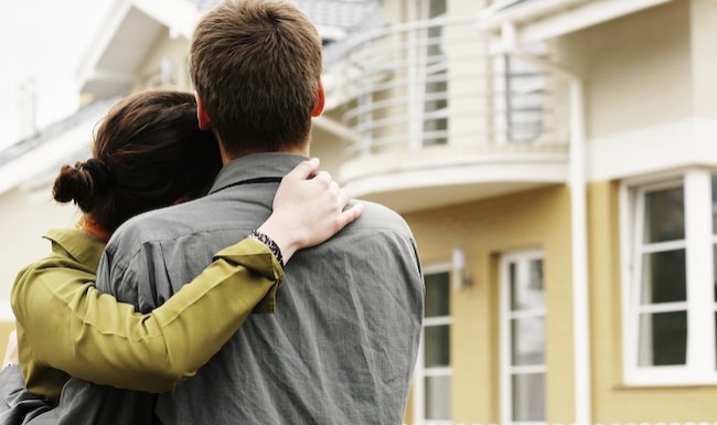 young couple in front of a tan home with white accents